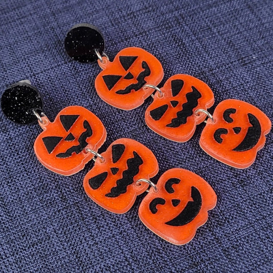 Halloween-themed earrings with jack-o'-lantern design on a blue textured background