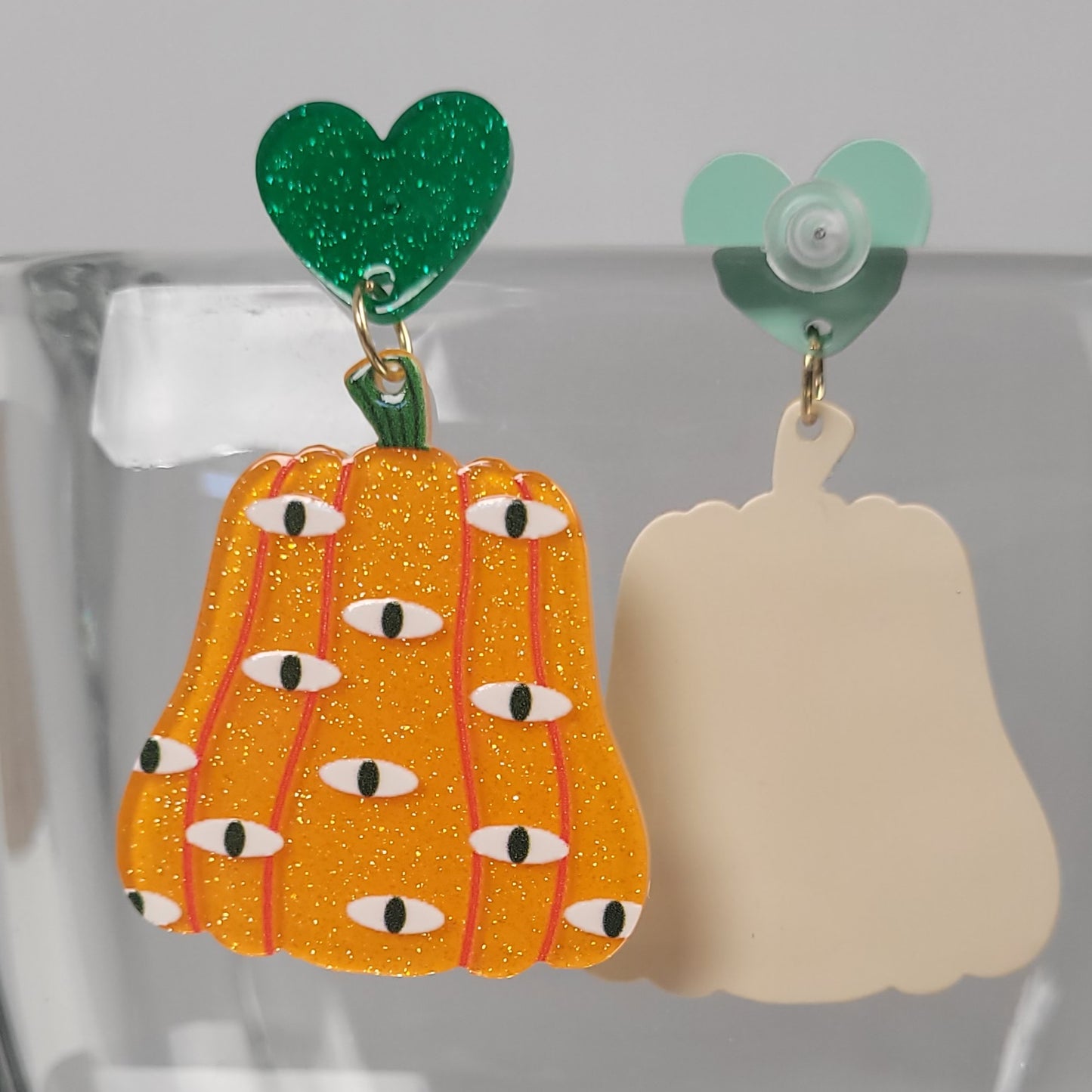 Pumpkin-shaped earrings with green tops multiple evil eyes on a clear stand.