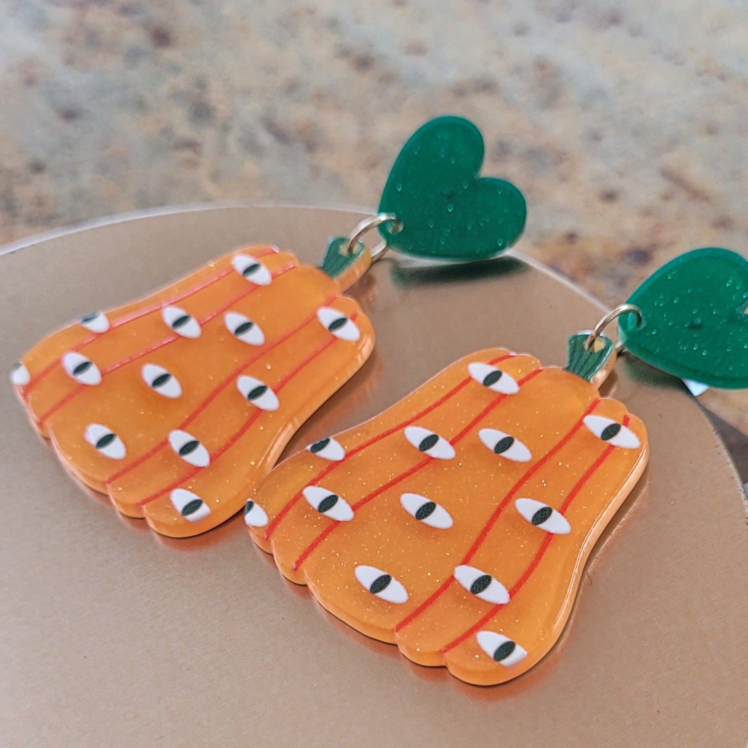 Pumpkin-shaped earrings with green Hearts on a beige background