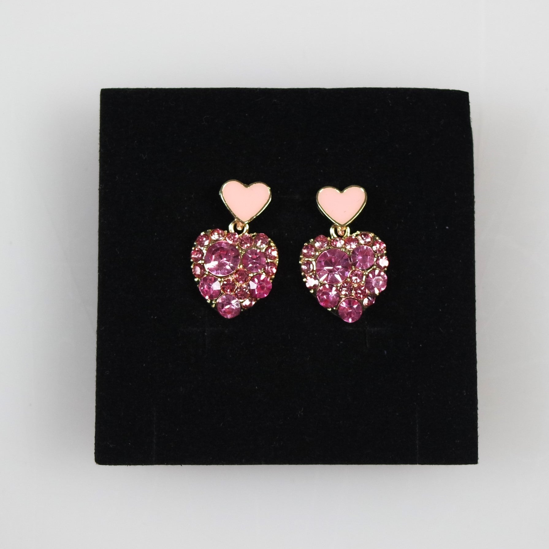 Heart-shaped earrings with pink gemstones on a black stand.