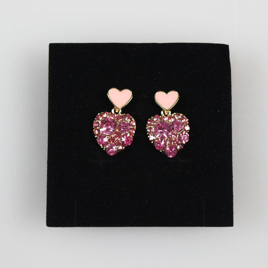 Heart-shaped earrings with pink gemstones on a black stand.