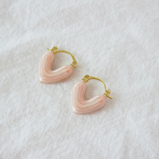 A pair of heart-shaped, gold-tone huggie earrings with a pink oil drip effect, displayed on a white background.