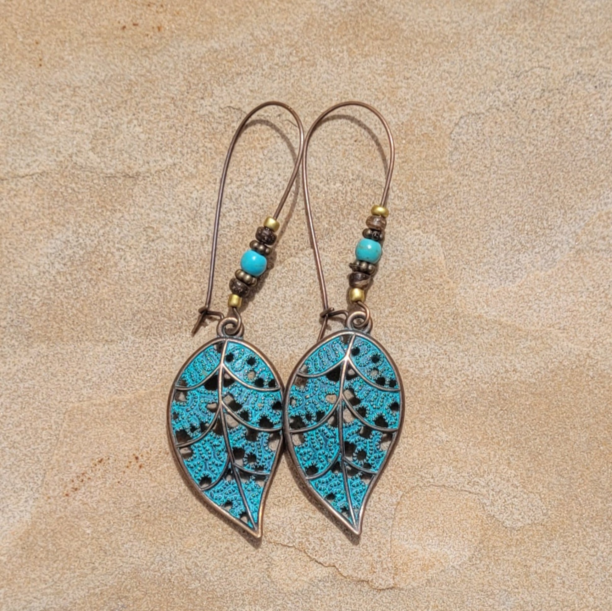 Pair of earrings with turquoise leaf-shaped stones on a beige background