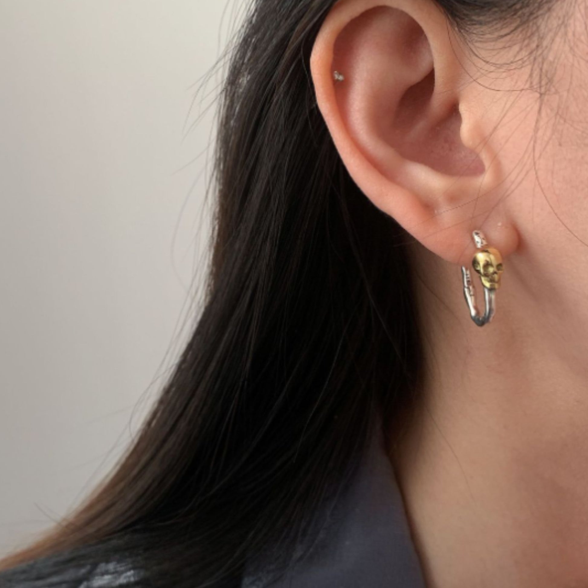 Close-up of an ear wearing a gold and silver hoop earring against a neutral background