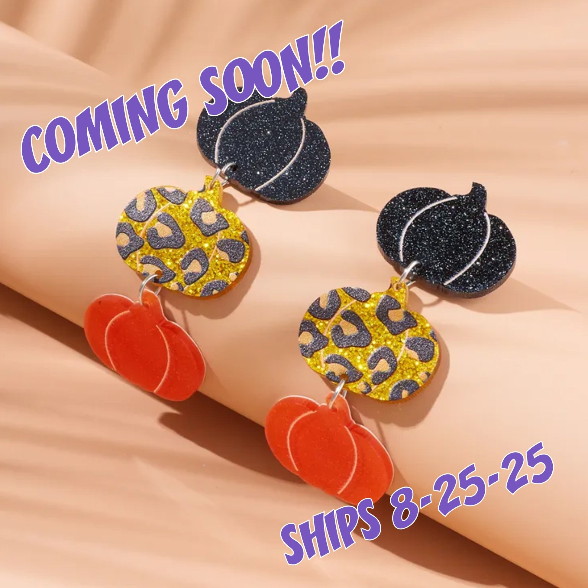 Halloween-themed earrings with pumpkins and glittery leaves on a beige background, with text indicating 'Coming Soon' and 'Ships 8-25-25'.