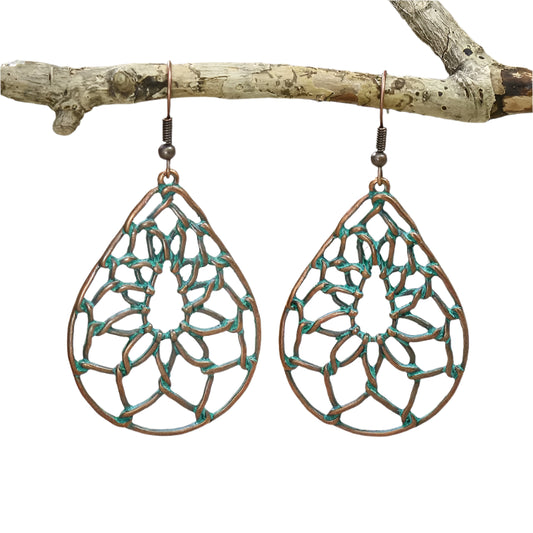 A pair of teardrop dangle earrings with a Native Bohemian dream catcher net design in antique brass and green finish, displayed on a branch.
