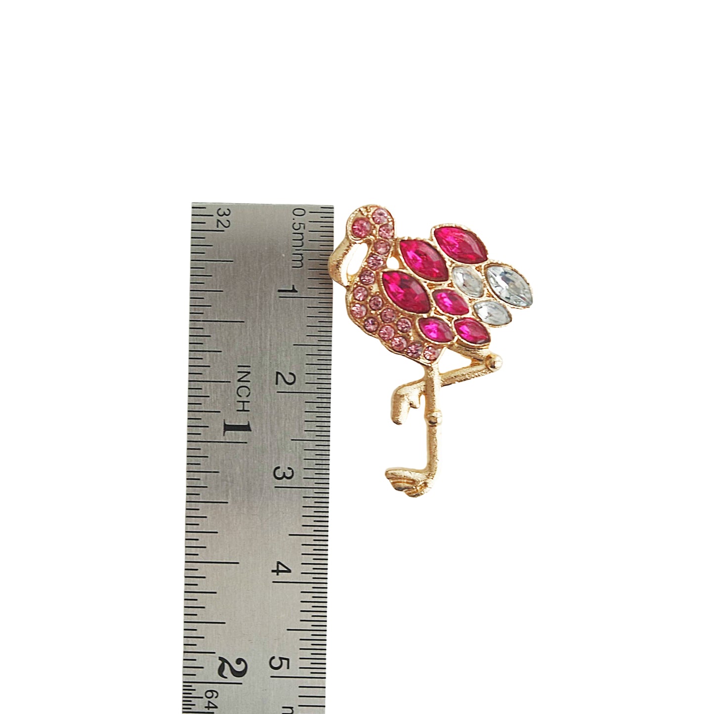 Flamingo-shaped brooch with pink and white gemstones next to a ruler for scale on a white background