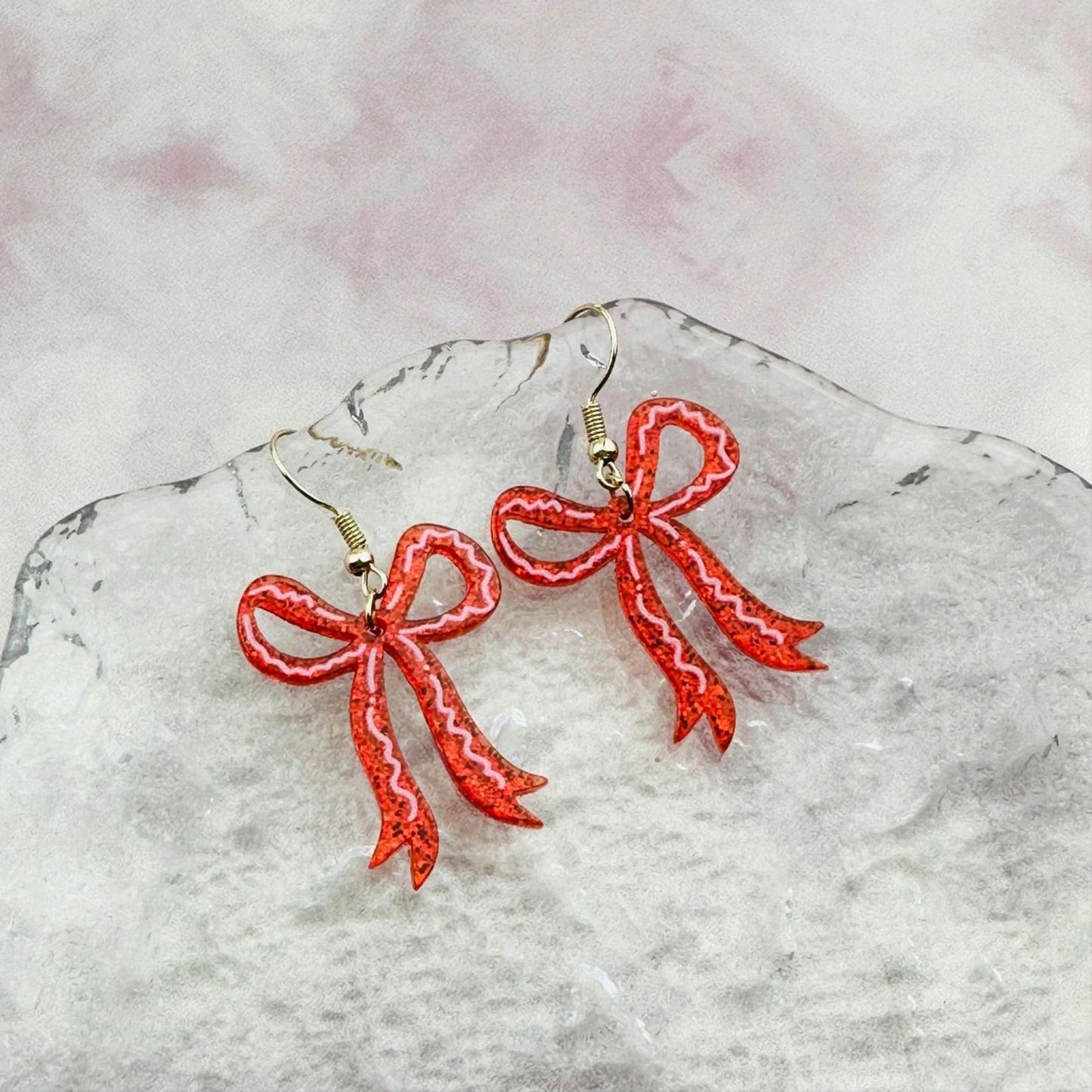 Red bow-shaped earrings on a marble surface