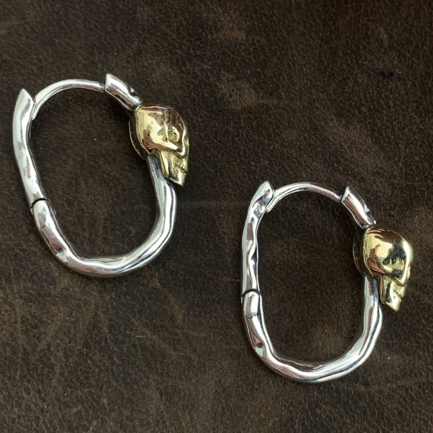 Pair of silver hoop earrings with gold accents on a brown background