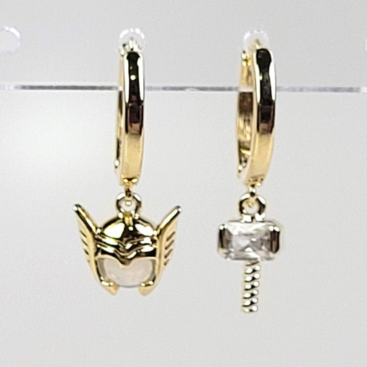 Gold hoop earrings with superhero mask and hammer design on a clear stand.
