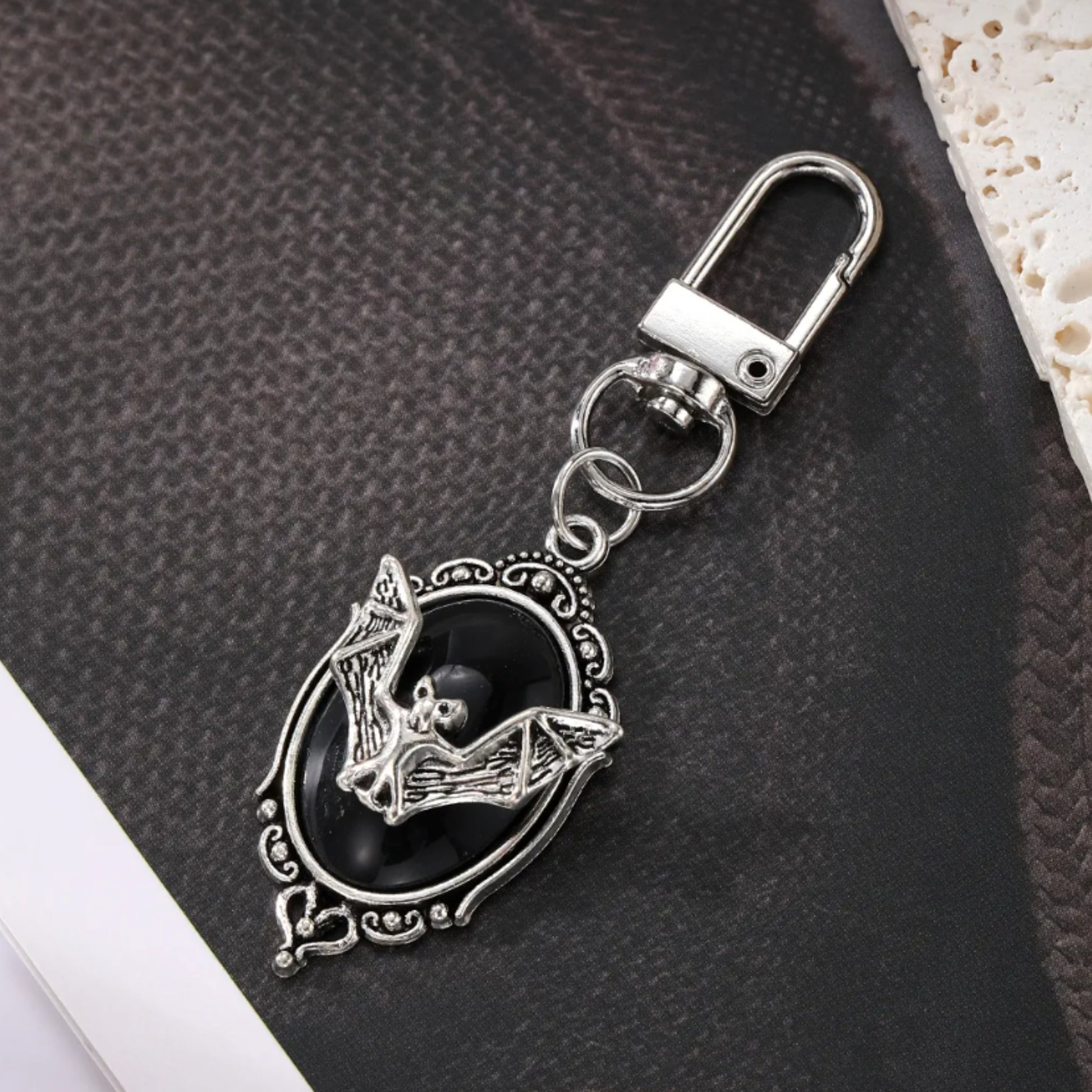 Decorative keychain with black stone and silver bat metalwork on a textured surface