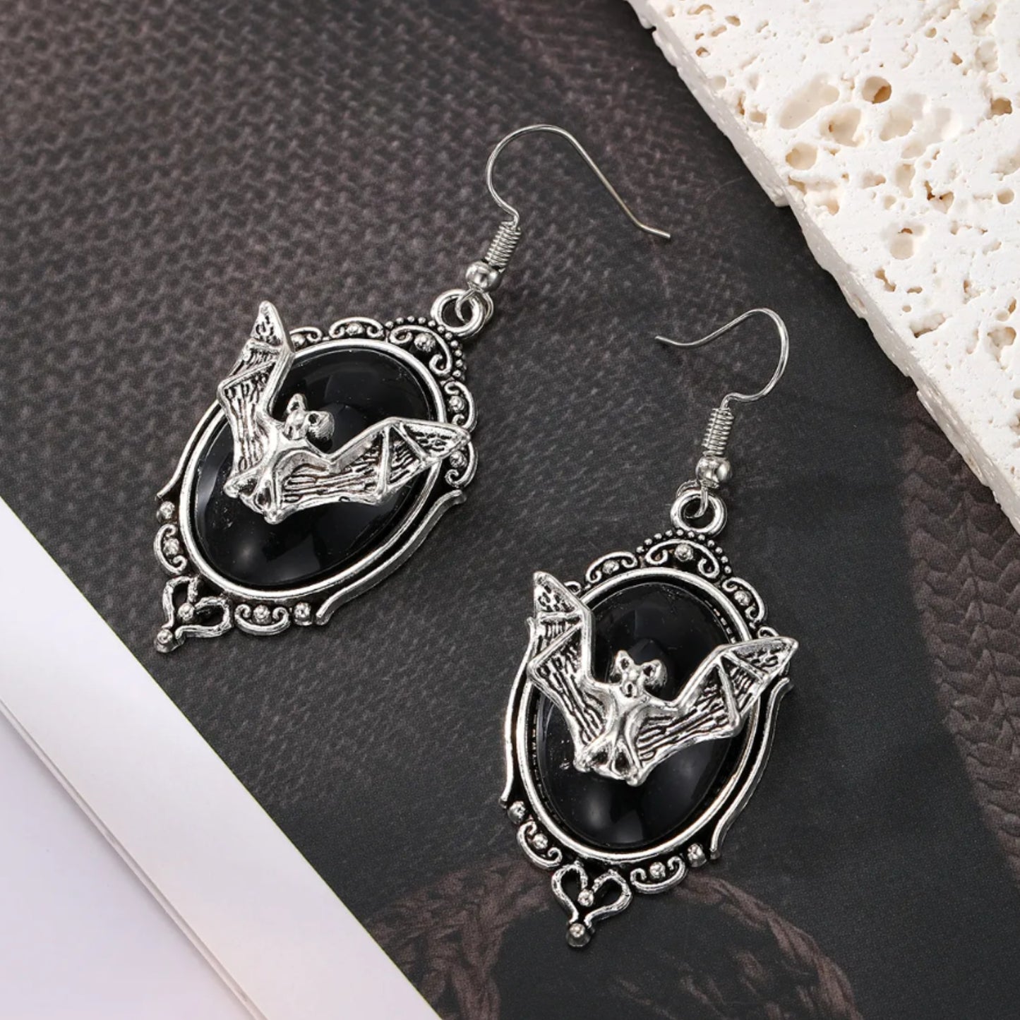 Pair of silver bat earrings on a textured surface