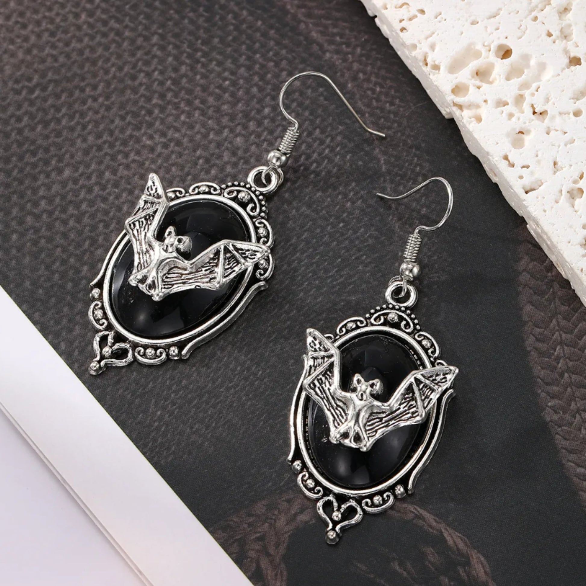 Pair of silver bat earrings on a textured surface