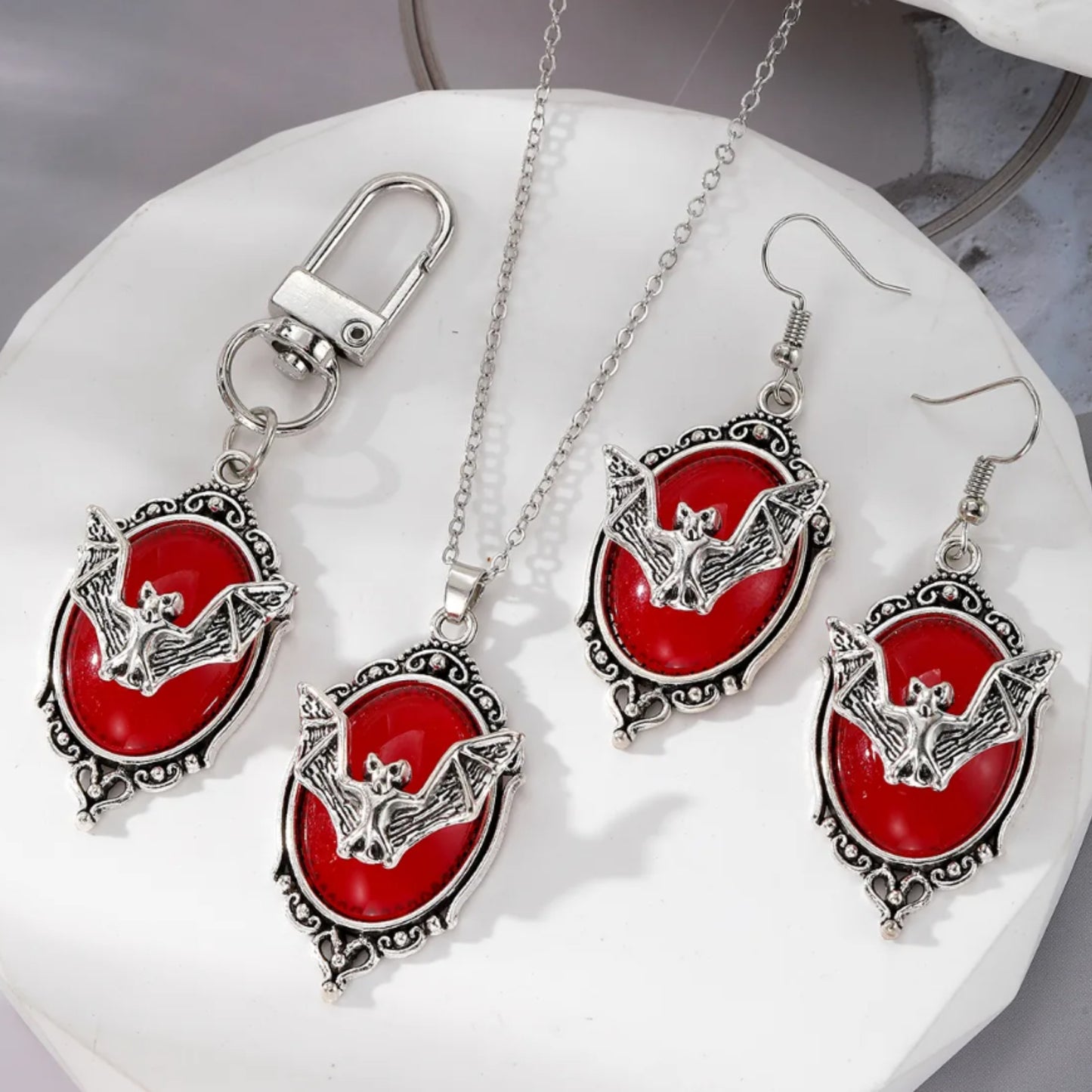 Jewelry set with red bat-themed pendants on a white surface