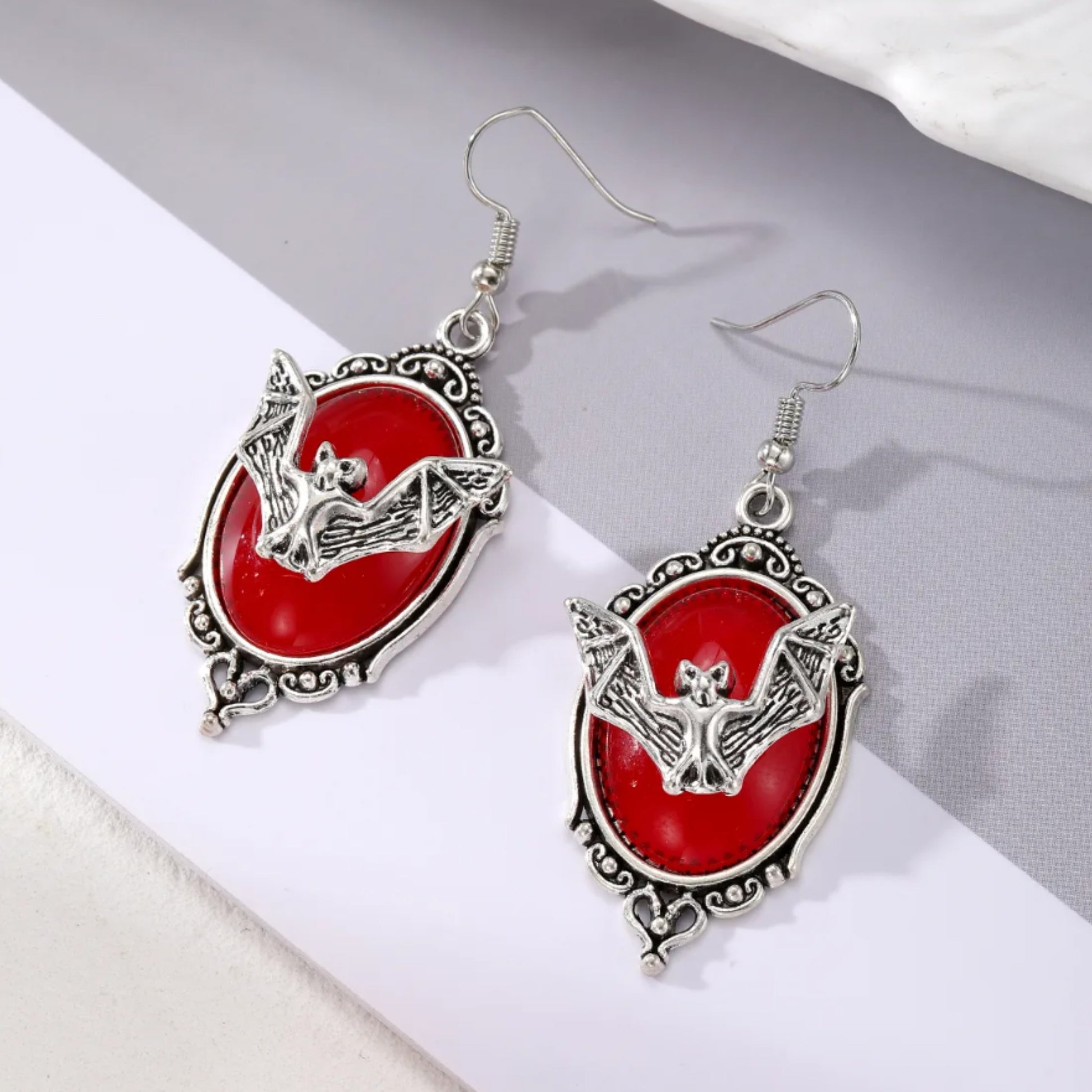 Pair of earrings with red oval stones and silver bat designs on a white surface.