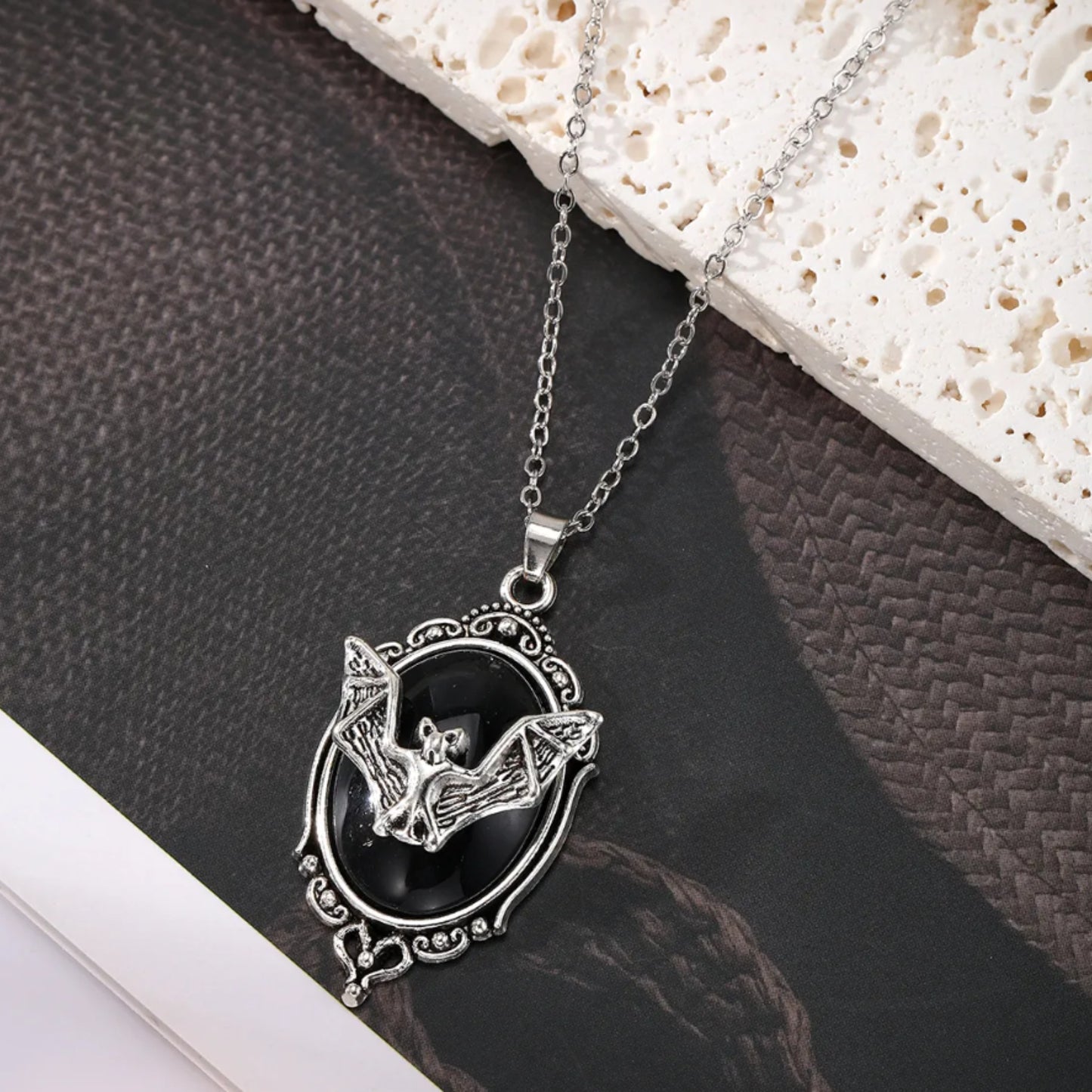 Silver necklace with a bat pendant on a textured surface