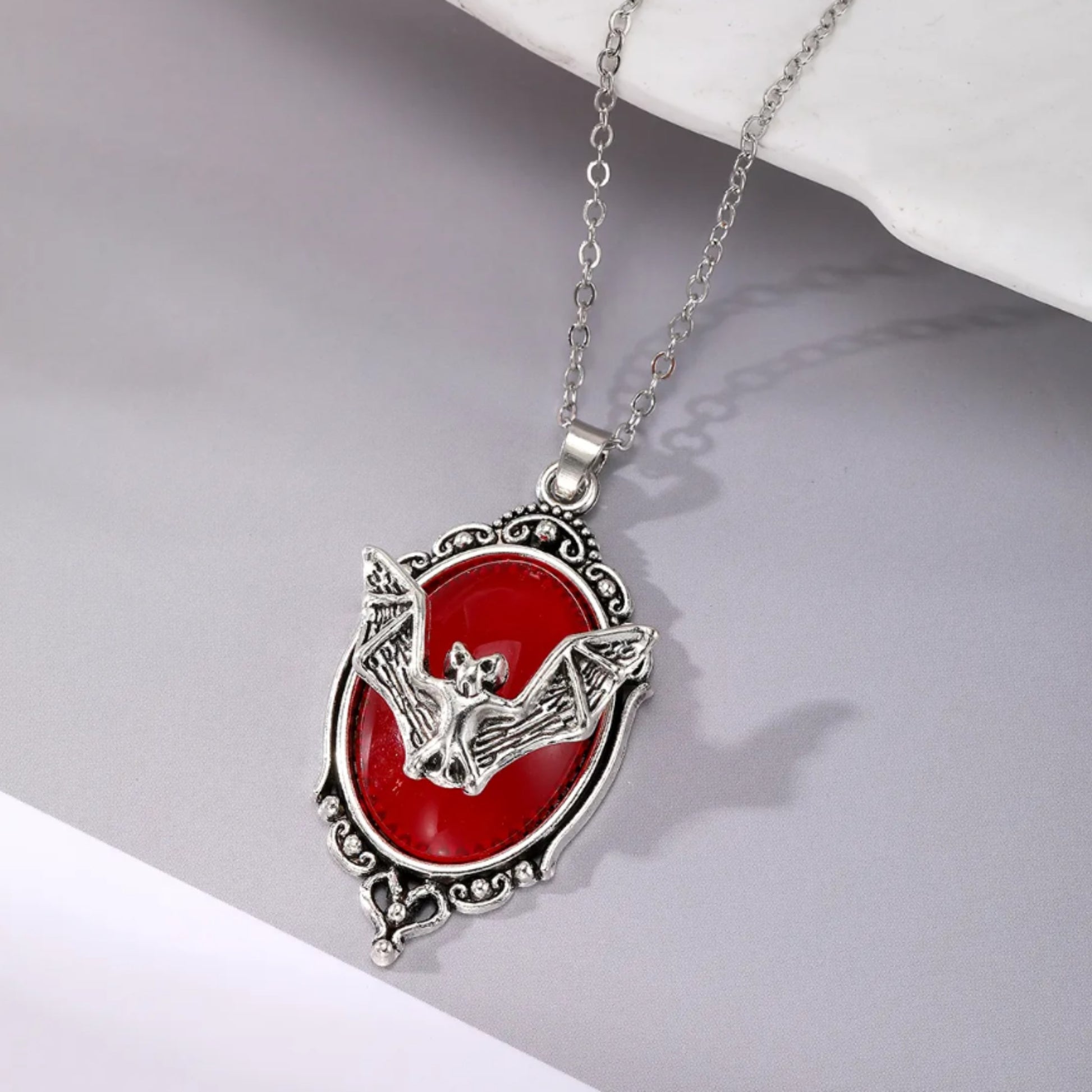 Necklace with a red pendant featuring a bat design on a gray surface.